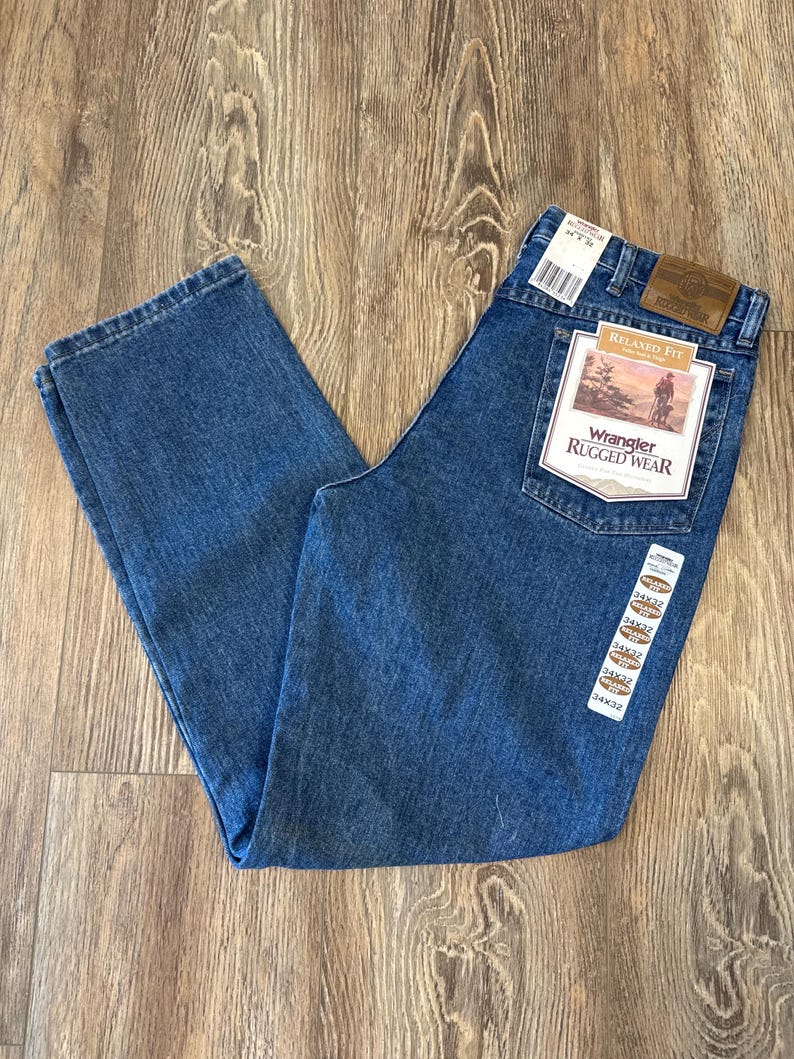 May include: A pair of blue denim jeans with a brown leather Wrangler Rugged Wear label. The label has the text "Relaxed Fit" and a picture of a cowboy riding a horse.