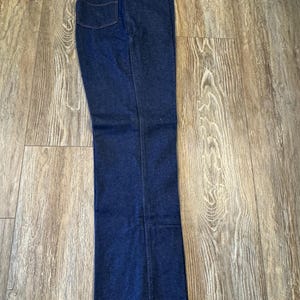 May include: Dark blue denim jeans with a tag attached. The jeans have a classic five-pocket design and a straight leg. The denim is a deep indigo color.