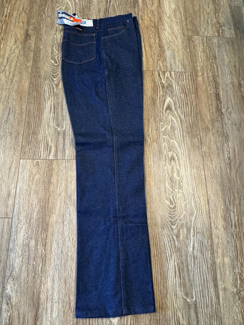 May include: Dark blue denim jeans with a tag attached. The jeans have a classic five-pocket design and a straight leg. The denim is a deep indigo color.