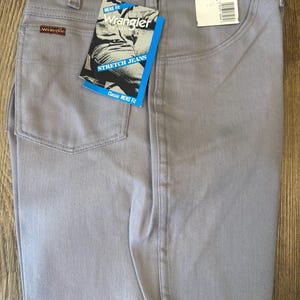 May include: Light gray Wrangler stretch jeans with a classic fit. The jeans have a straight leg and feature a tag with the Wrangler logo and the words "Stretch Jeans". The jeans are size 36 x 34.