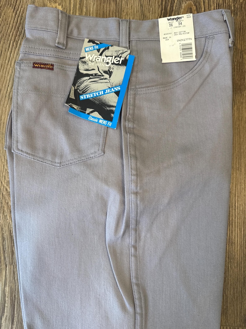 May include: Light gray Wrangler stretch jeans with a classic fit. The jeans have a straight leg and feature a tag with the Wrangler logo and the words "Stretch Jeans". The jeans are size 36 x 34.