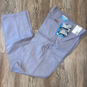 May include: Light blue Wrangler Flex Fit waist stretch jeans. The jeans have a classic fit and feature a tag with the Wrangler logo and product information. The pants are laid out on a wooden surface.