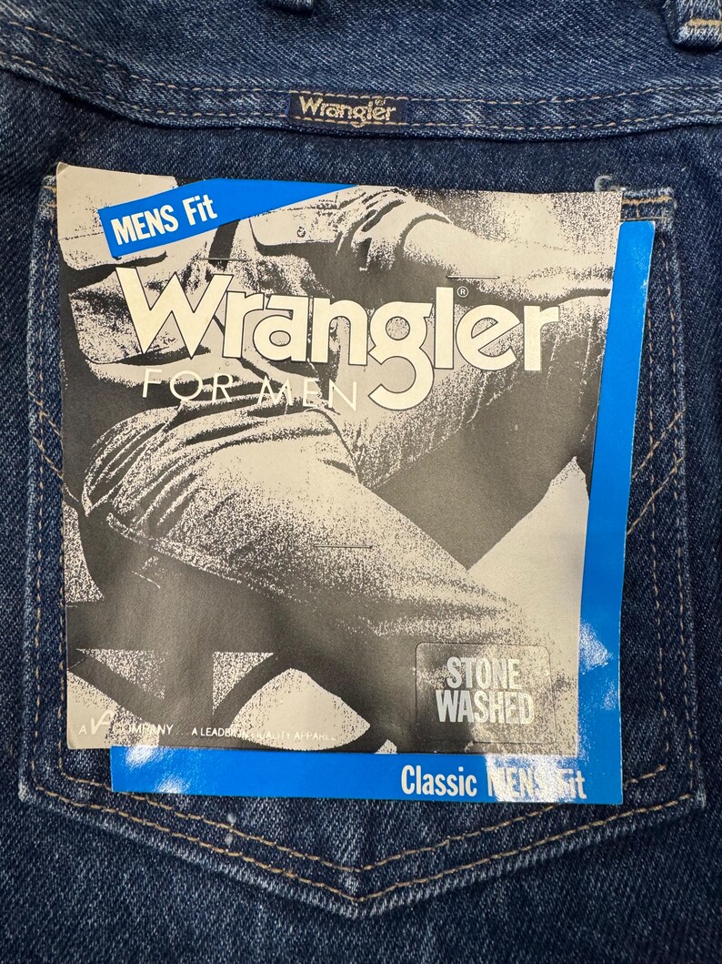 K&ouml;nnte beinhalten: Nahaufnahme einer blauen Jeans mit einem Wrangler-Etikett auf der Ges&auml;&szlig;tasche. Das Etikett lautet "Wrangler FOR MEN" und "STONE WASHED". Die Jeans hat eine klassische Herrenpassform.