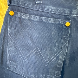 May include: A pair of dark blue denim jeans with a back pocket featuring a stitched W-shaped design and a small copper rivet.
