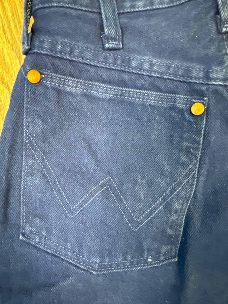 May include: A pair of dark blue denim jeans with a back pocket featuring a stitched W-shaped design and a small copper rivet.