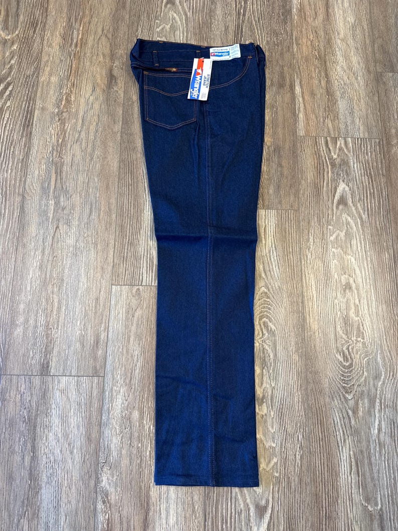 Peut inclure: Un jean en denim bleu fonc&eacute; avec une &eacute;tiquette Wrangler. Le jean a une coupe droite et un style classique &agrave; cinq poches.
