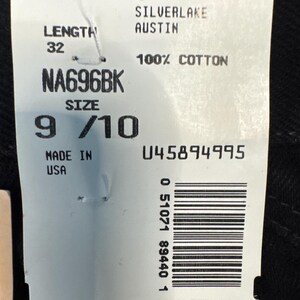 May include: A white tag with the Wrangler logo and product information. The tag reads "SILVERLAKE AUSTIN" and "100% COTTON". It also indicates a length of 32 and a size of 9/10. The tag is marked "MADE IN USA".