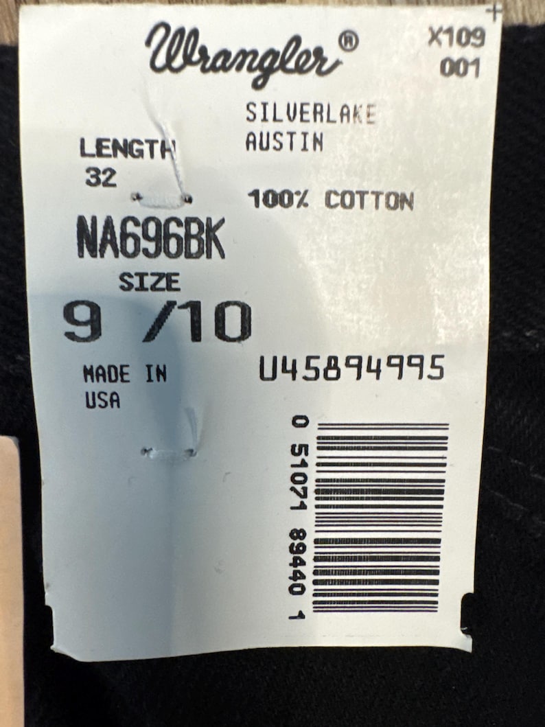 May include: A white tag with the Wrangler logo and product information. The tag reads "SILVERLAKE AUSTIN" and "100% COTTON". It also indicates a length of 32 and a size of 9/10. The tag is marked "MADE IN USA".