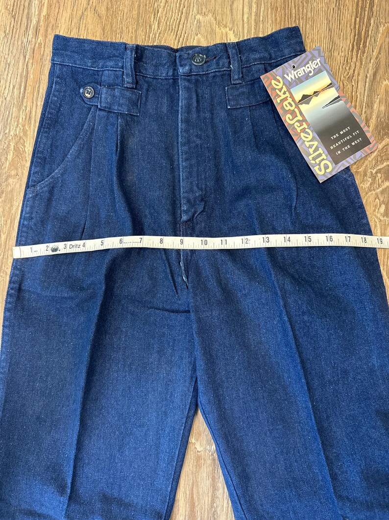 Puede incluir: Pantalones vaqueros azul oscuro con cintura alta y pliegues. Los pantalones tienen cierre de bot&oacute;n y un peque&ntilde;o bolsillo. Una etiqueta dice "Silverlake" y "Wrangler". Los pantalones miden aproximadamente 48 cm en la cintura.