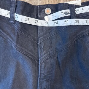 K&ouml;nnte beinhalten: Schwarze Jeans aus Denim mit hoher Taille und geradem Bein. Die Jeans hat ein einzigartiges Design mit N&auml;hten an den vorderen Taschen und einem Knopfverschluss. Die Taille wird mit einem Ma&szlig;band gemessen und zeigt eine Gr&ouml;&szlig;e von 68,58 cm.