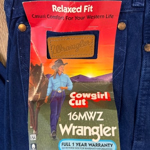 May include: A blue pair of Wrangler jeans with a tag that reads "Relaxed Fit Casual Comfort For Your Western Life." The tag also features a brown leather Wrangler logo, a cowgirl riding a horse, and the text "Cowgirl Cut 16MWZ Wrangler Full 1 Year Warranty See Reverse Side For Warranty Information."