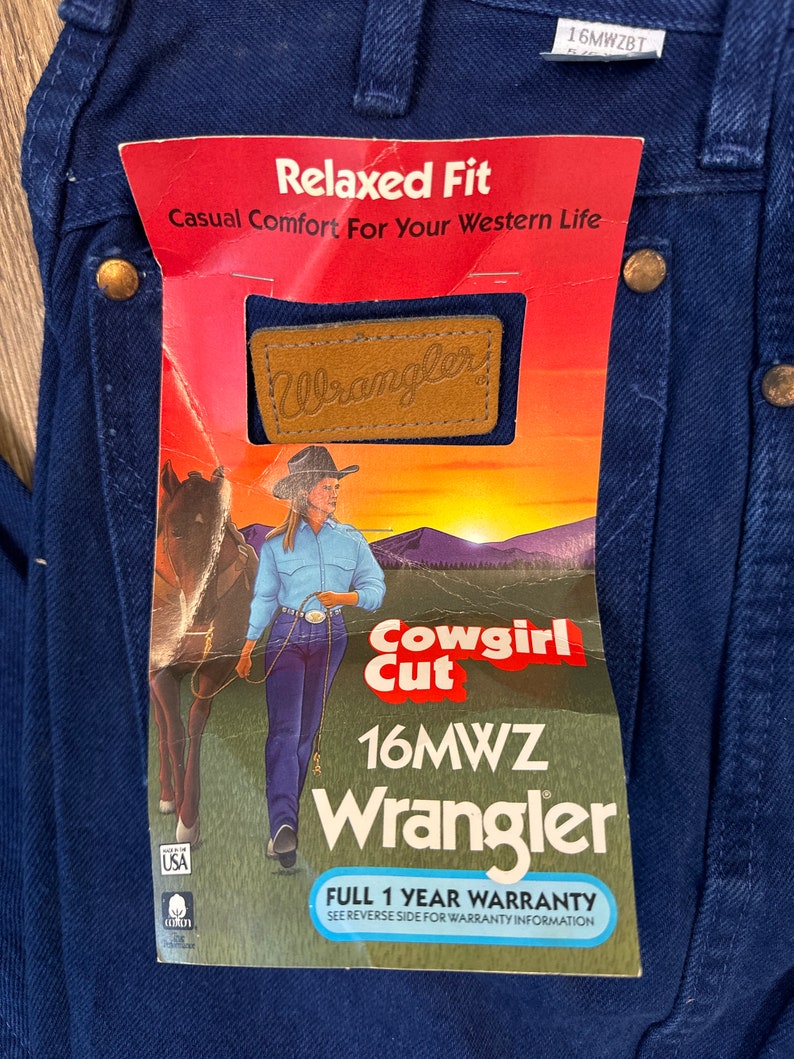 May include: A blue pair of Wrangler jeans with a tag that reads "Relaxed Fit Casual Comfort For Your Western Life." The tag also features a brown leather Wrangler logo, a cowgirl riding a horse, and the text "Cowgirl Cut 16MWZ Wrangler Full 1 Year Warranty See Reverse Side For Warranty Information."