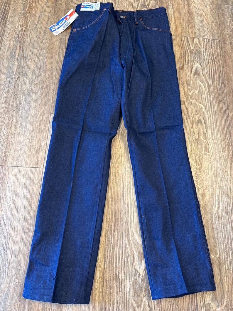 Peut inclure: Un jean en denim bleu fonc&eacute; avec une &eacute;tiquette Wrangler. Le jean a une jambe droite et une coupe classique &agrave; cinq poches.
