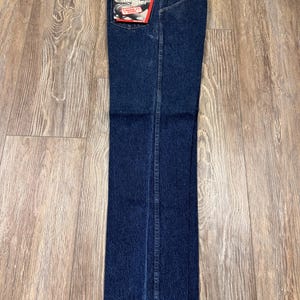 May include: Dark blue denim jeans with a classic straight leg fit. The jeans have a Wrangler brand label on the back pocket and a brown leather patch at the waistband. The jeans are new with tags.