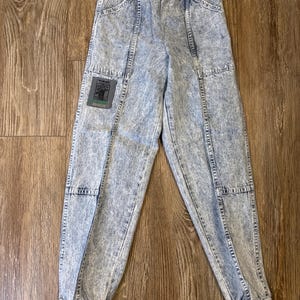 K&ouml;nnte beinhalten: Jeanshose mit S&auml;urewaschung, elastischem Bund und einem Aufn&auml;her am linken Bein. Die Hose hat einen hellblauen und wei&szlig;en Marmoreffekt. Die Hose hat Taschen und ist an den Kn&ouml;cheln ger&uuml;scht. Ein Etikett ist am Bund befestigt.