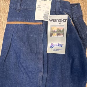 Puede incluir: Un par de pantalones vaqueros azules con una cintura de cuero marr&oacute;n. Los vaqueros tienen una etiqueta que dice "Wrangler Silverlake" y "The most beautiful fit in the West".