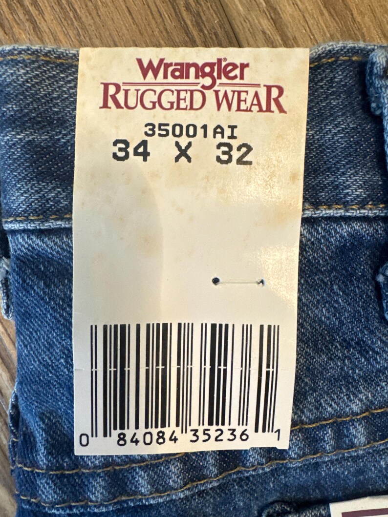 May include: A white tag with black text that reads "Wrangler Rugged Wear 35001A1 34 x 32" and a barcode with the number "0 84084 35236 1".