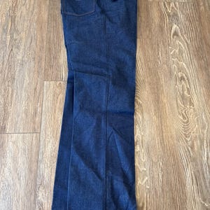 May include: A pair of dark blue denim jeans with a Wrangler tag attached. The jeans have a straight leg fit and a classic five-pocket style.