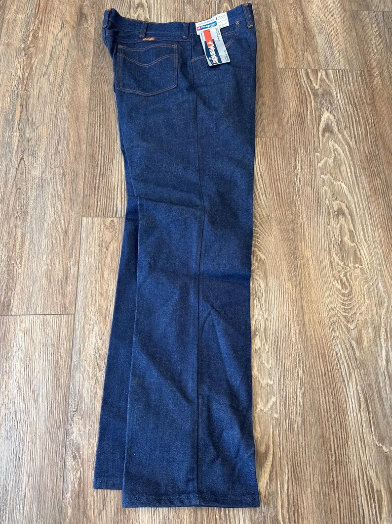 May include: A pair of dark blue denim jeans with a Wrangler tag attached. The jeans have a straight leg fit and a classic five-pocket style.