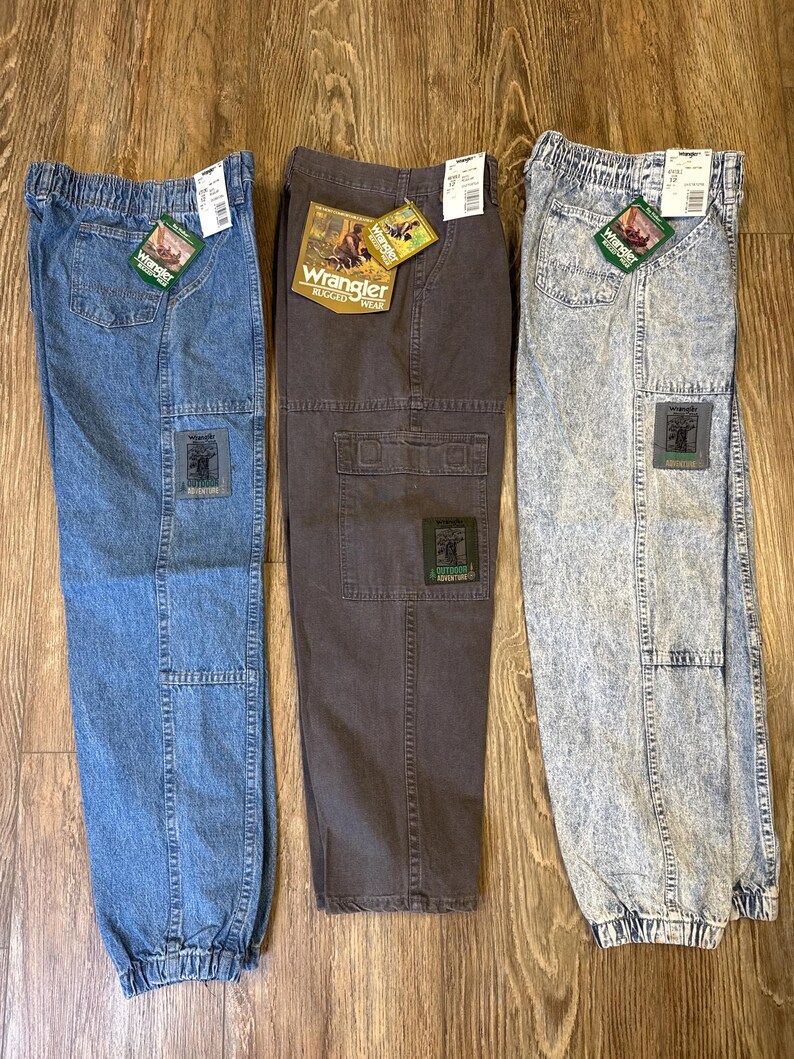 K&ouml;nnte beinhalten: Drei Wrangler Rugged Wear Cargo-Hosen in blauem Denim, Braun und Acid-Wash-Denim. Jede Hose hat einen Aufn&auml;her am Bein und ein Etikett. Die Hosen haben einen elastischen Bund und B&uuml;ndchen.