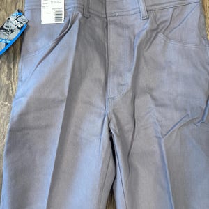 May include: Light gray Wrangler jeans with a tag attached. The tag displays the brand name and size information. The jeans have a classic five-pocket design and a straight leg cut. The fabric appears to be a durable denim material.