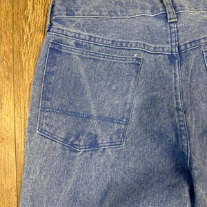 May include: Close-up of the back of light blue denim jeans. The jeans have a single back pocket and a waistband with belt loops. The denim has a faded appearance, with lighter areas creating a worn look. The stitching is visible along the seams and pocket edges.