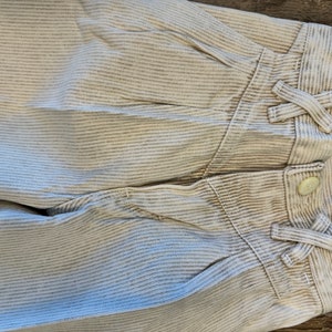 May include: A pair of white corduroy trousers with a striped pattern. The trousers have a button fastening and a tie at the waist.
