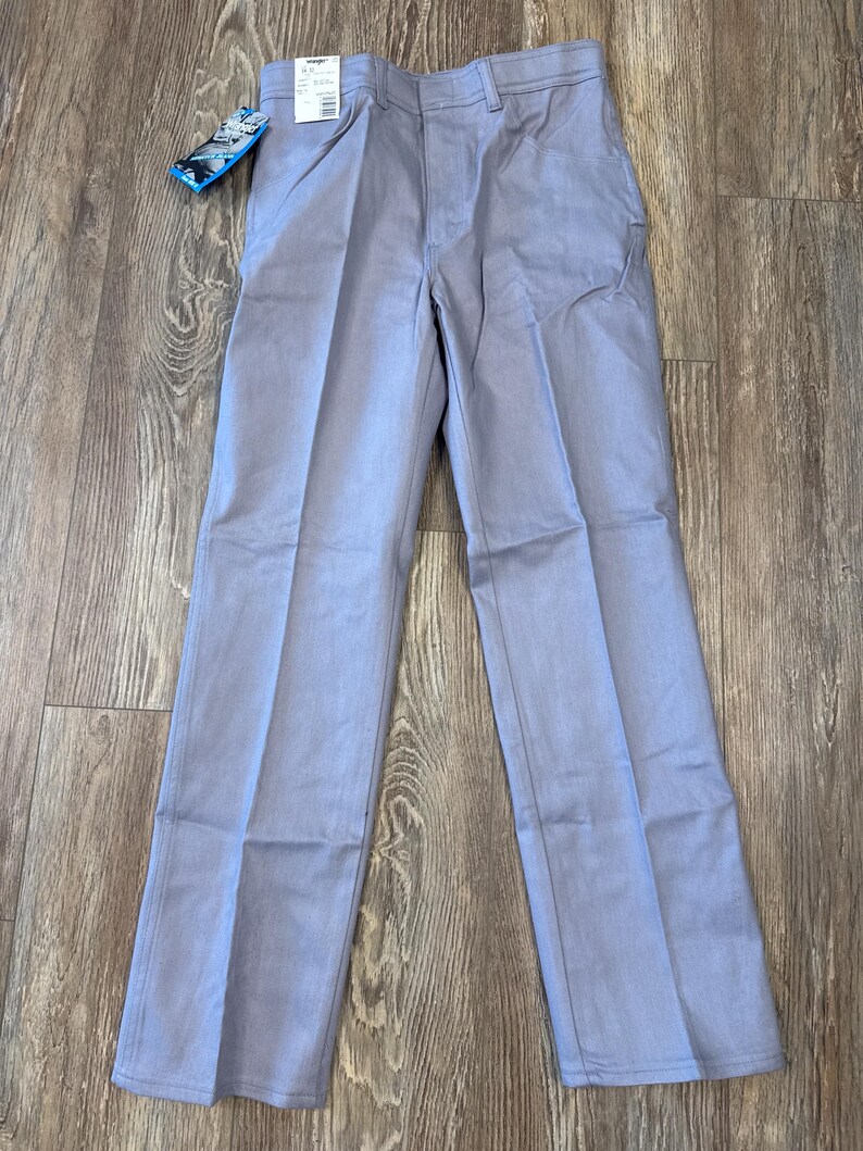 May include: Light blue Wrangler pants with a straight leg design. The pants have a classic five-pocket style and a tag attached to the waistband. The pants are made of a durable fabric and are suitable for everyday wear.