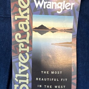 Puede incluir: Etiqueta de mezclilla azul de jeans Wrangler. La etiqueta presenta el nombre de la marca, una imagen de paisaje y el texto "Silverlake". Tambi&eacute;n es visible el texto "The Most Beautiful Fit in the West".