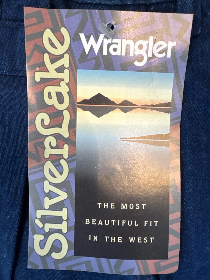 Puede incluir: Etiqueta de mezclilla azul de jeans Wrangler. La etiqueta presenta el nombre de la marca, una imagen de paisaje y el texto "Silverlake". Tambi&eacute;n es visible el texto "The Most Beautiful Fit in the West".