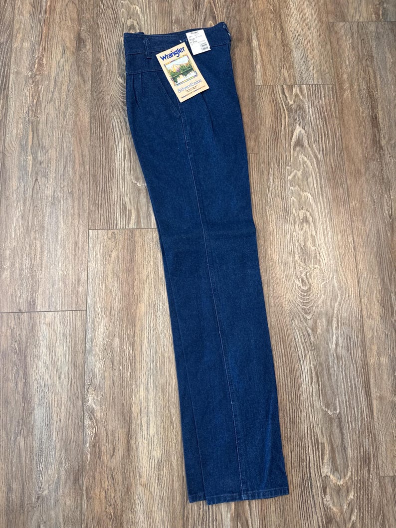 Puede incluir: Vaqueros Wrangler de mezclilla azul oscuro con cintura alta y pernera recta. Los vaqueros tienen una etiqueta que dice "Wrangler" y "Silverlake Vintage". Los vaqueros son nuevos con etiquetas.
