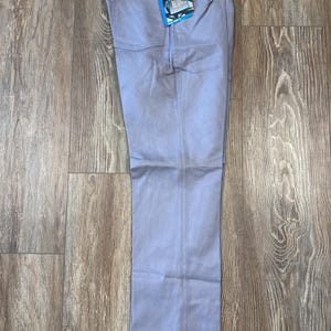 May include: Light blue Wrangler Flex Fit jeans with a straight leg. The jeans have a classic five-pocket design and a tag attached to the front. The jeans are laid flat on a wooden surface.