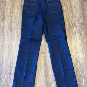 Peut inclure: Un jean en denim bleu fonc&eacute; &agrave; jambe droite. Le jean a un &eacute;cusson en cuir marron sur la ceinture arri&egrave;re avec le mot "Wrangler" imprim&eacute; dessus. Le jean a une &eacute;tiquette attach&eacute;e &agrave; la ceinture arri&egrave;re qui dit "Genuine Western Jeans" et "Wrangler".