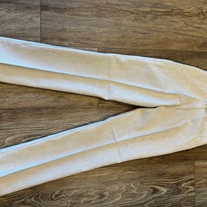 May include: A pair of white striped Wrangler jeans with a size tag attached. The jeans are laid flat on a wooden surface.