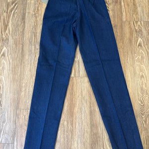 Puede incluir: Pantalones vaqueros azul oscuro con cintura alta y pernera recta. Los pantalones tienen un dise&ntilde;o cl&aacute;sico de cinco bolsillos y una peque&ntilde;a etiqueta de marca en la parte trasera. Una etiqueta de precio est&aacute; adherida a la cintura.