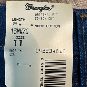 May include: A white tag with black text that reads "Wrangler", "Original Fit Cowboy Cut", "Length 34", "13MWZG Size 11", "100% Cotton", "Made in USA", and "042234815". A barcode is also visible on the tag.