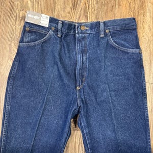 K&ouml;nnte beinhalten: Nahaufnahme einer blauen Wrangler-Jeans. Die Jeans hat ein klassisches F&uuml;nf-Taschen-Design, einen Knopf- und Rei&szlig;verschluss und eine gerade Beinpassform. Das Etikett lautet "Wrangler 34x36".