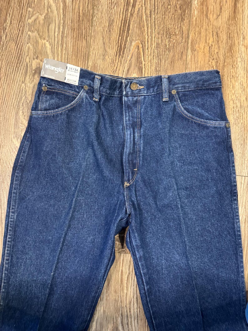 K&ouml;nnte beinhalten: Nahaufnahme einer blauen Wrangler-Jeans. Die Jeans hat ein klassisches F&uuml;nf-Taschen-Design, einen Knopf- und Rei&szlig;verschluss und eine gerade Beinpassform. Das Etikett lautet "Wrangler 34x36".