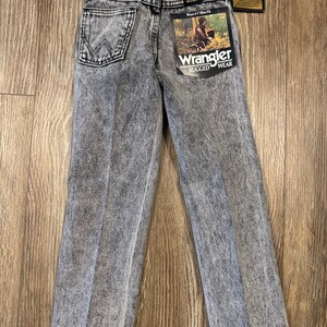 Puede incluir: Un par de pantalones vaqueros grises lavados con &aacute;cido con una etiqueta de Wrangler. Los vaqueros son de corte ajustado y tienen un dise&ntilde;o cl&aacute;sico de cinco bolsillos.