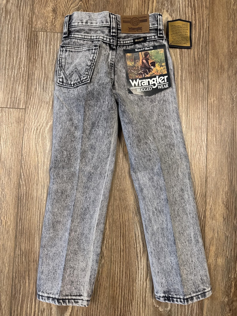 Puede incluir: Un par de pantalones vaqueros grises lavados con &aacute;cido con una etiqueta de Wrangler. Los vaqueros son de corte ajustado y tienen un dise&ntilde;o cl&aacute;sico de cinco bolsillos.