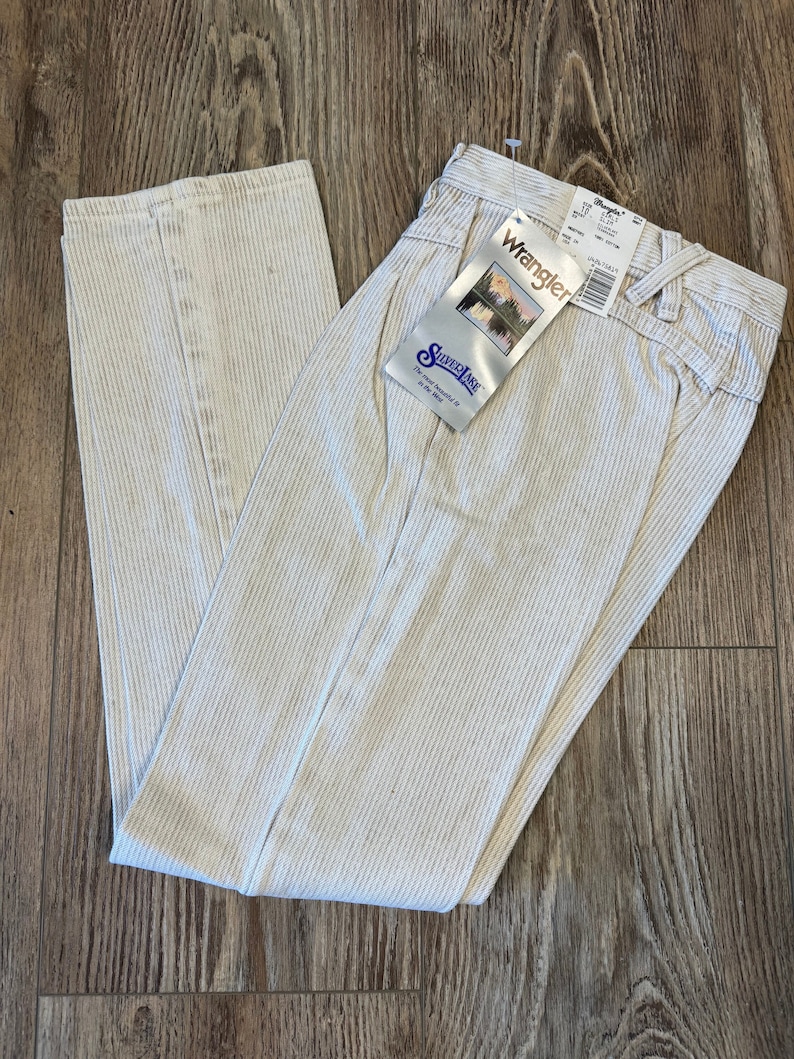May include: A pair of off-white corduroy trousers with a subtle striped pattern. The trousers have a straight leg and a zip fly. The Wrangler brand label is attached to the trousers.