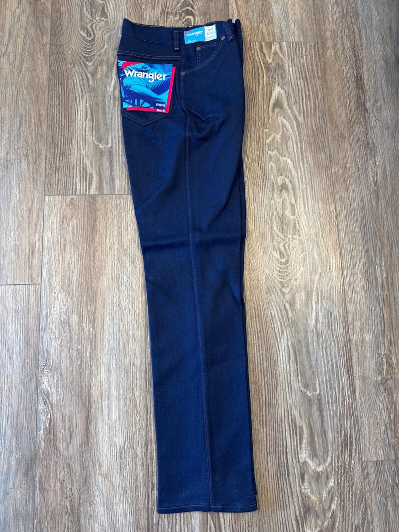 K&ouml;nnte beinhalten: Dunkelblaue Jeans aus Denim mit einem Wrangler-Etikett auf der Ges&auml;&szlig;tasche.