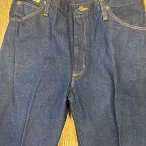 May include: Dark blue classic jeans with a straight leg cut. The jeans have a button and zipper closure, front and back pockets, and yellow stitching. A tag reads "CLASSIC JEANS" and "34x34".