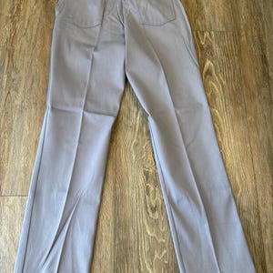 May include: Light blue pants with two back pockets and a small tag. The pants are made of a durable material and have a classic, straight-leg design. The pants are laid out on a wooden surface.