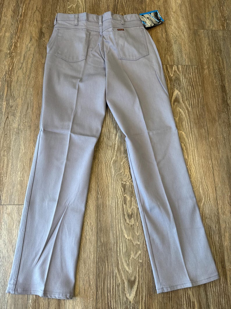 May include: Light blue pants with two back pockets and a small tag. The pants are made of a durable material and have a classic, straight-leg design. The pants are laid out on a wooden surface.