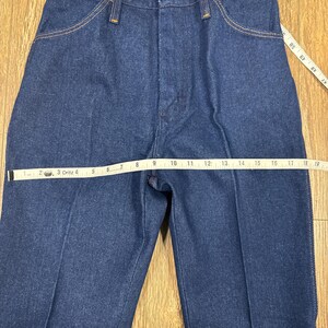 K&ouml;nnte beinhalten: Nahaufnahme einer blauen Jeans mit Knopfverschluss und Taschen. Ein Ma&szlig;band zeigt die Bundweite. Die Jeans hat ein klassisches, gerades Bein-Design.