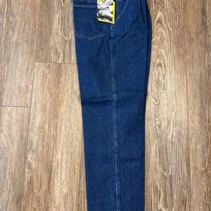 May include: Blue denim jeans with a straight leg. The jeans have a classic five-pocket design and a Wrangler brand label on the back waistband. The jeans are new with tags.