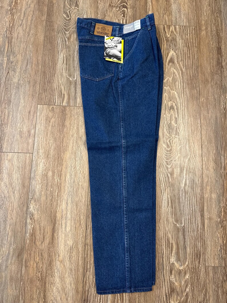 May include: Blue denim jeans with a straight leg. The jeans have a classic five-pocket design and a Wrangler brand label on the back waistband. The jeans are new with tags.