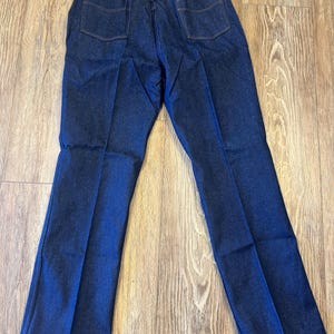 May include: Dark blue denim jeans with a classic five-pocket design. The jeans have a straight leg cut and feature a Wrangler tag. The back pockets have a stitched design. The jeans are made of a durable denim material.