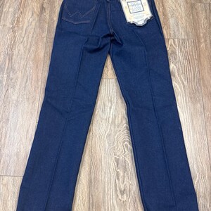 May include: Dark blue denim jeans with a classic fit. The jeans feature the Wrangler logo on the back pocket and a tag with the text "915 Classic Jeans". The jeans have a straight leg and are made of a durable denim material.